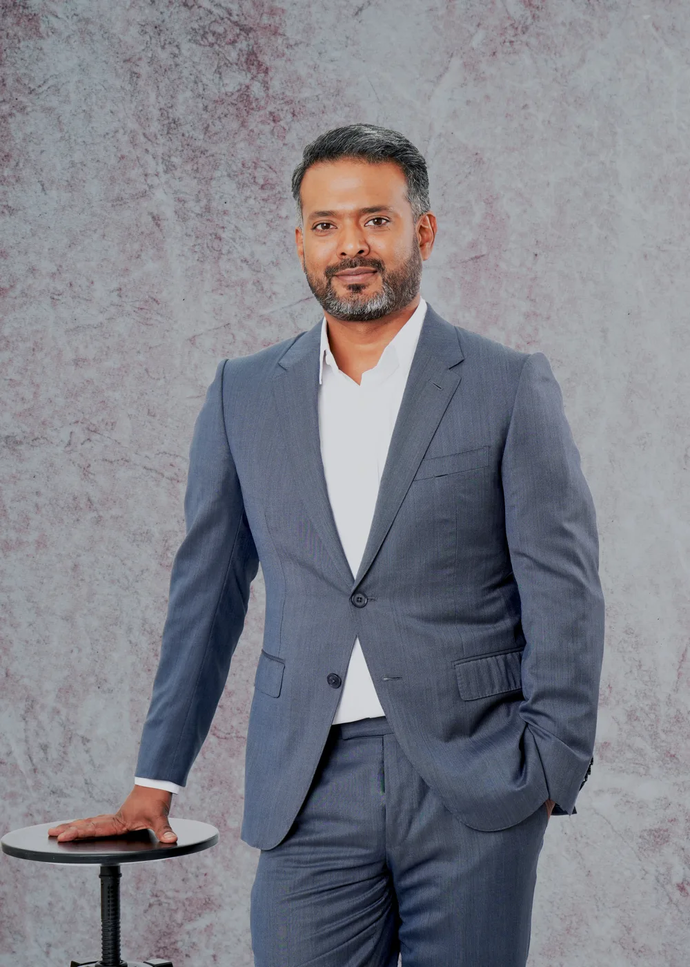 Ash Khan in a grey suit, smiling